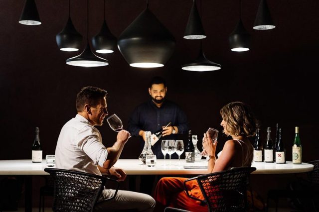 A group of people sitting at a table with wine bottles Description automatically generated with medium confidence