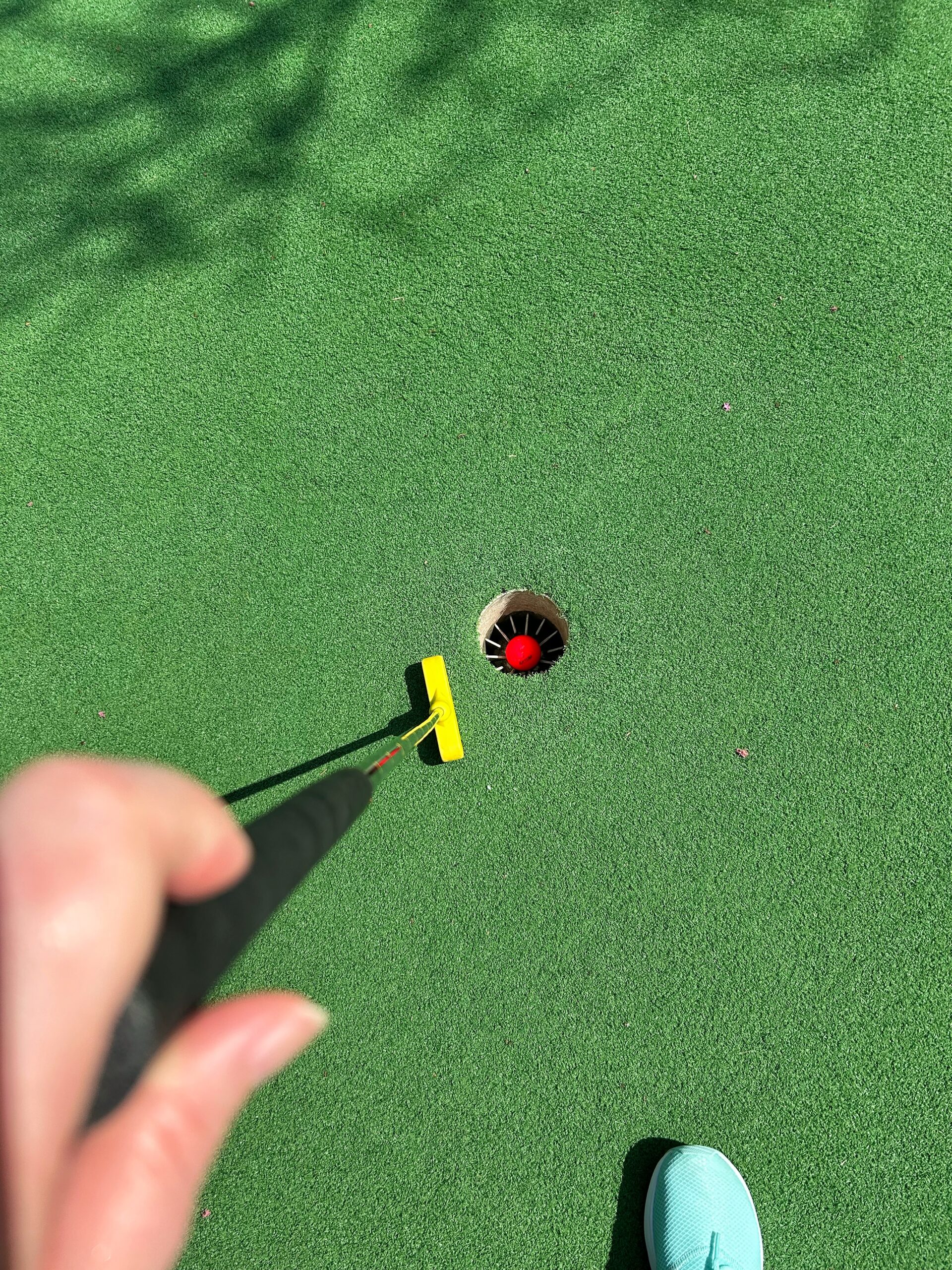 Red golf ball resting in the hole beside a putter after a winning shot.
