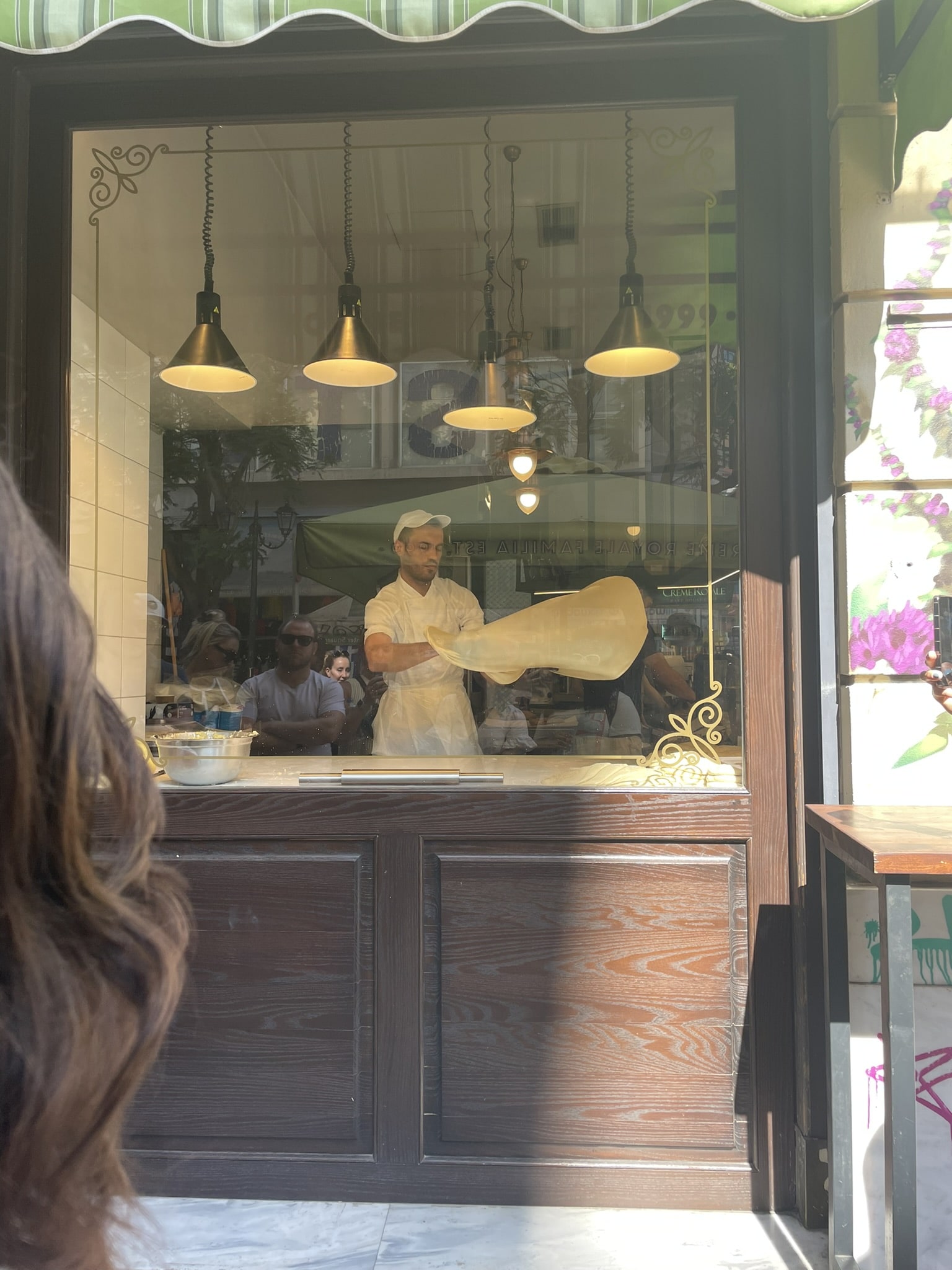 man in store window hand throwing a large sheet of dough