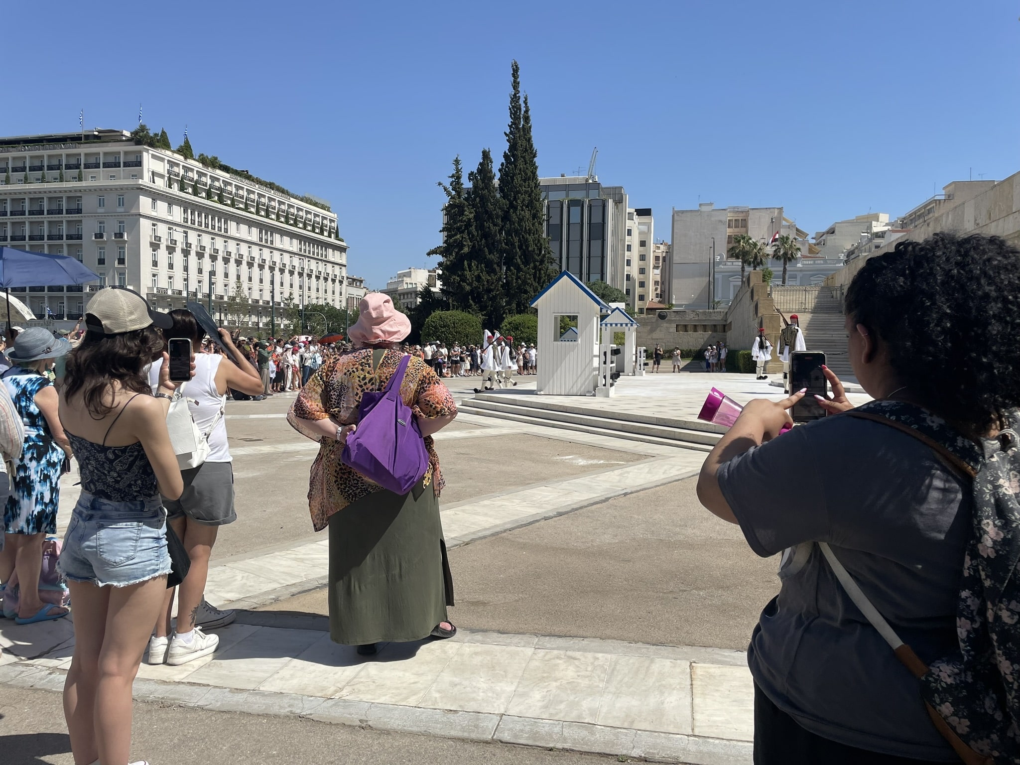 two teens holding up phones to photograph Greek guards