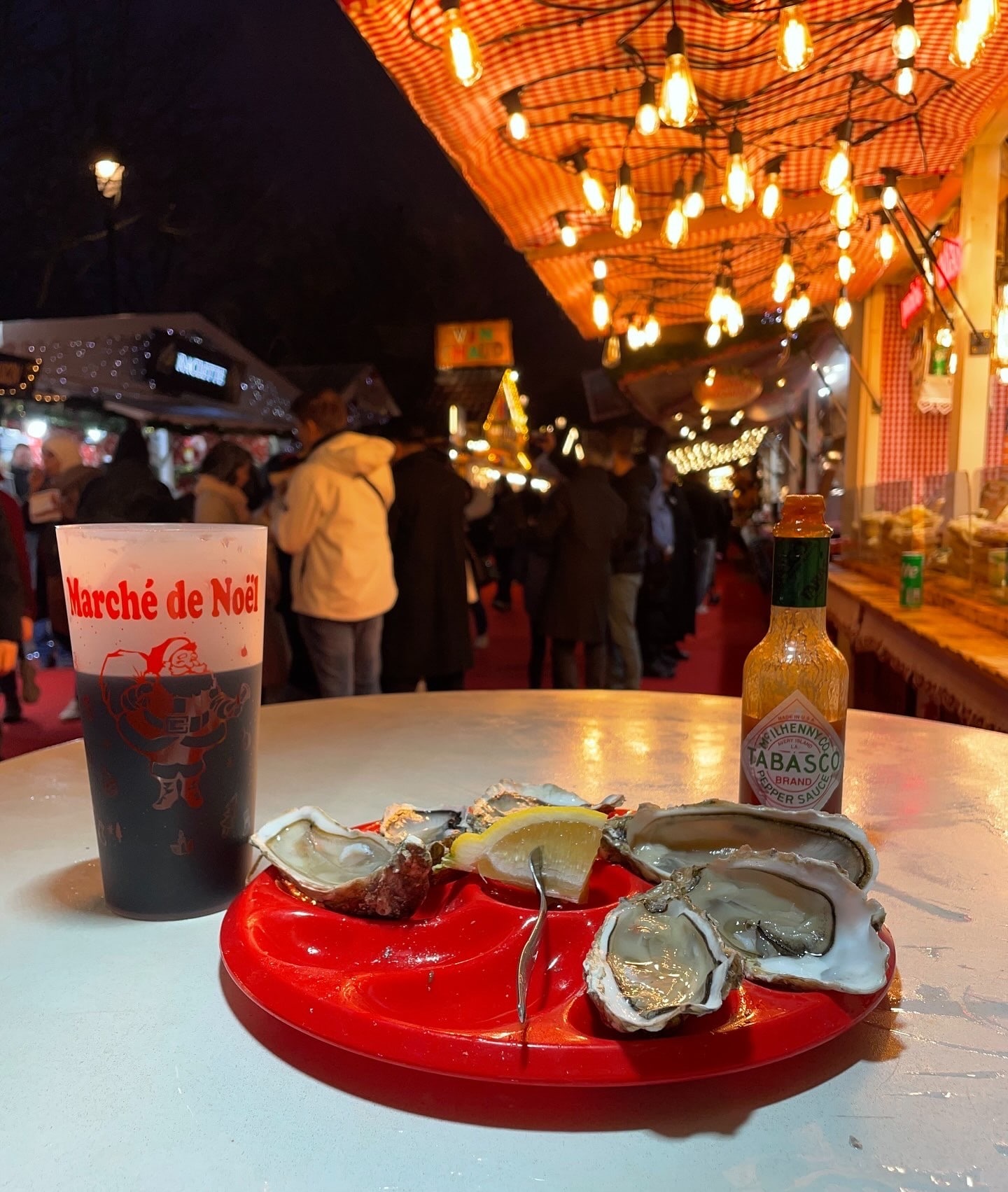Oysters on a plate with a cup full of dark red liquid that says "Marche de Noel" on the side