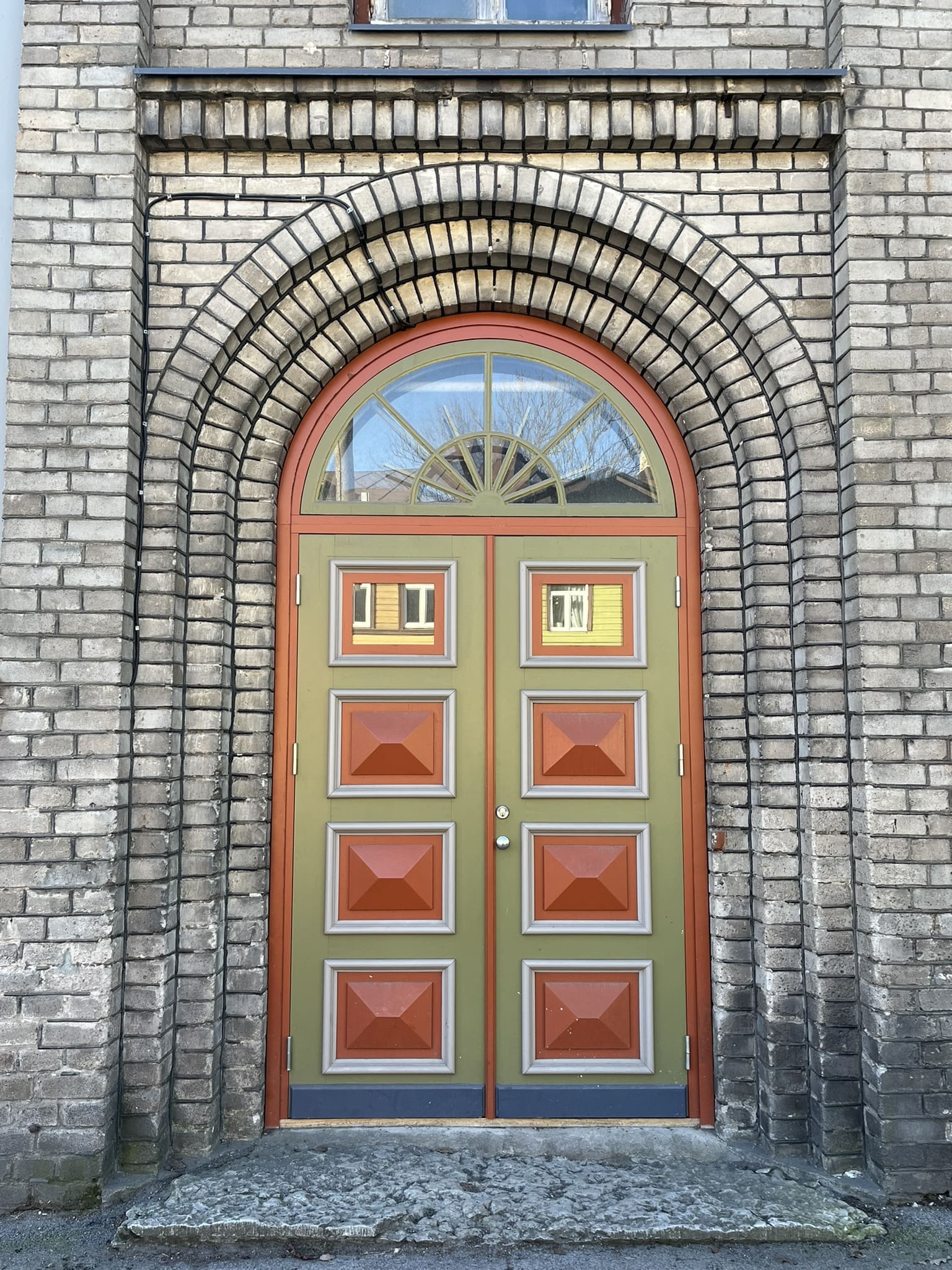 green and brown/red door set in rounded arch brick doorway