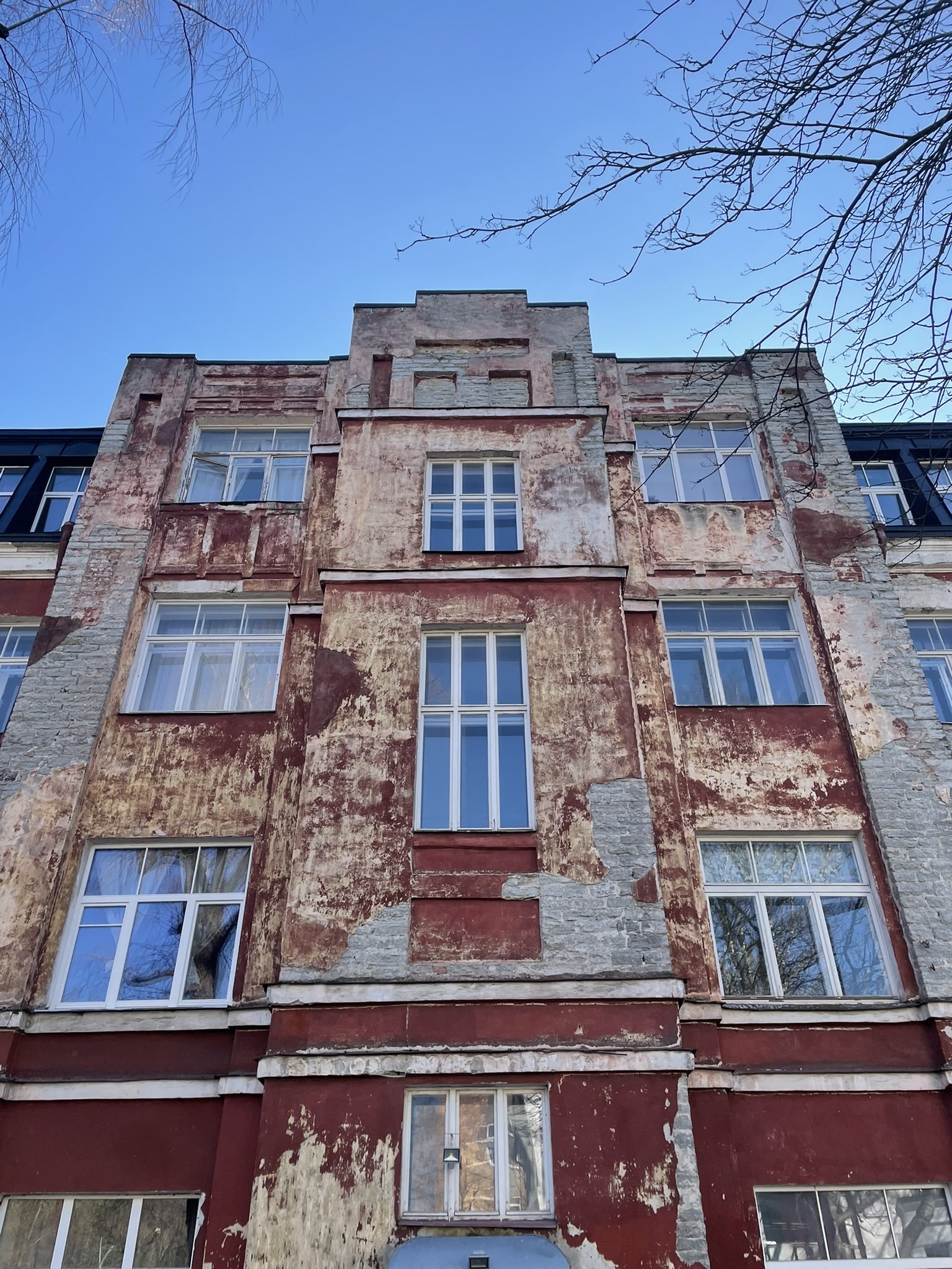 upwards view of a tall but run down cement and brick building with peeling red paint