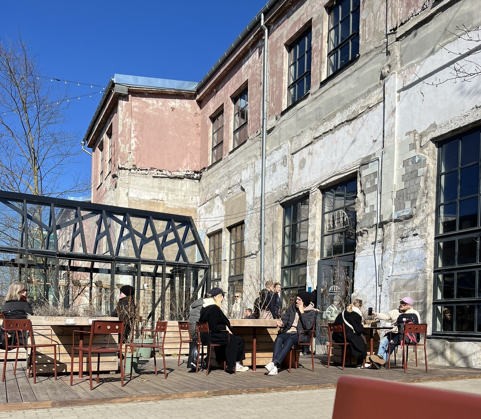 exterior view of run down concrete buildings, with people sitting at tables and chairs set out front