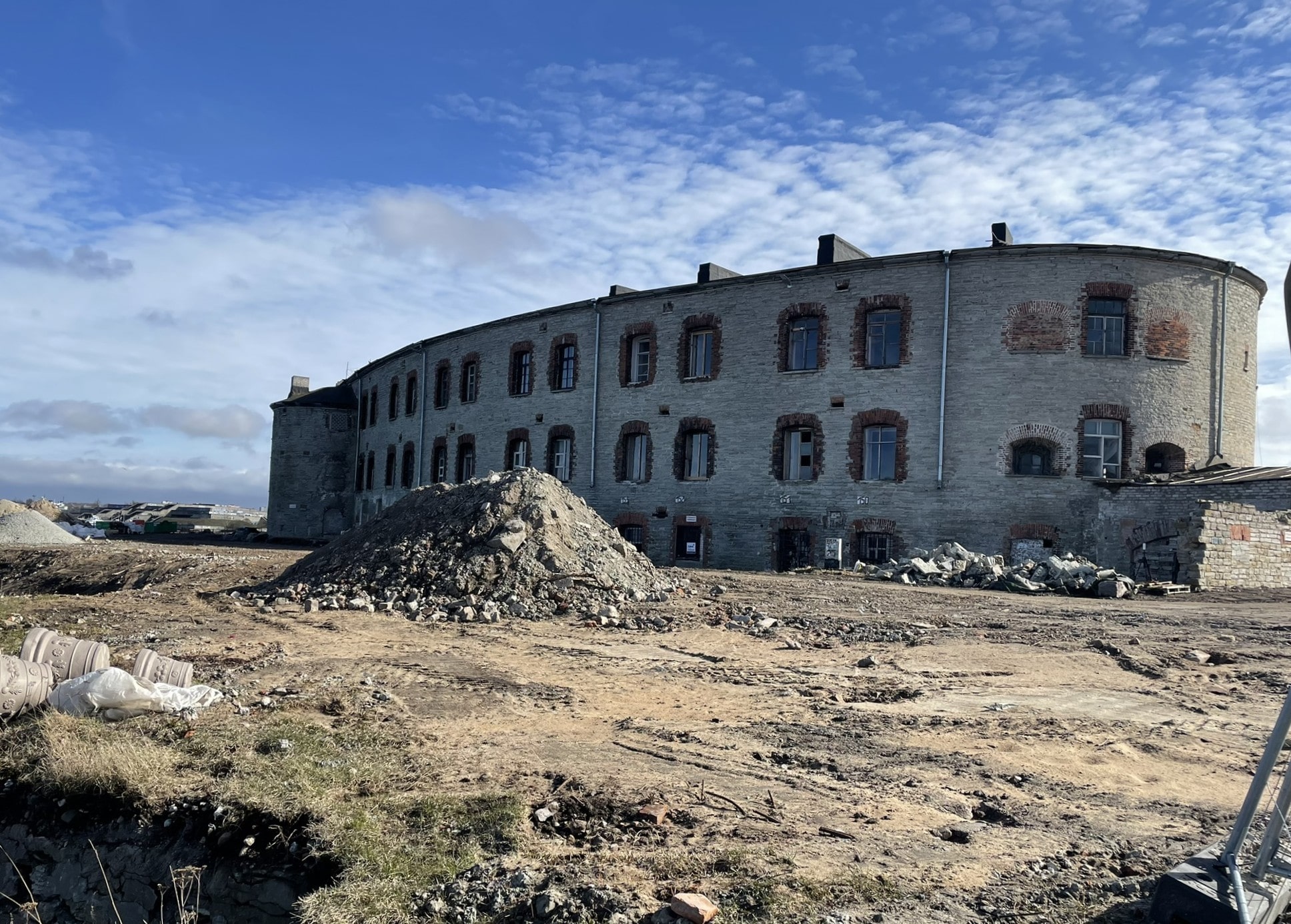 Long three story limestone building, curved at the end with a pile of construction dirt in the foreground