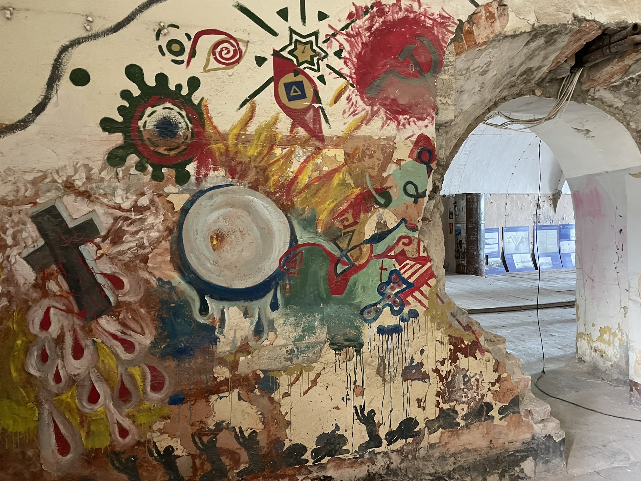 large wall mural painted on crumblin wall, featuring a cross, a hammer and sickle, a star, and other abstract designs