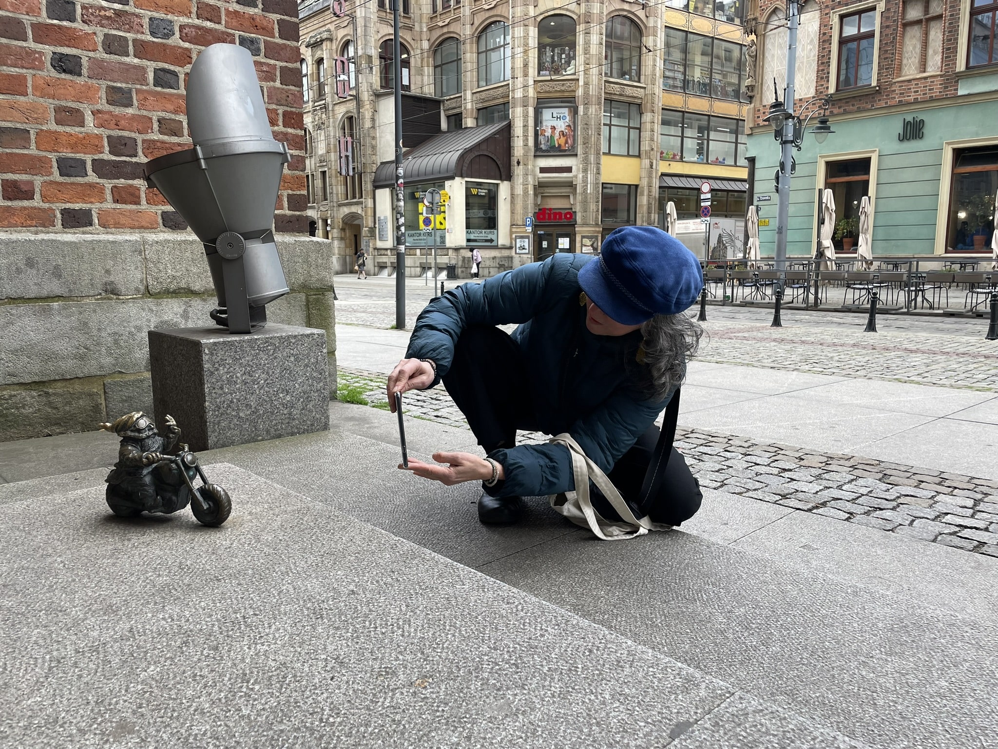 woman crouched down capturing a photo of a small statue of a gnome on a motorbike