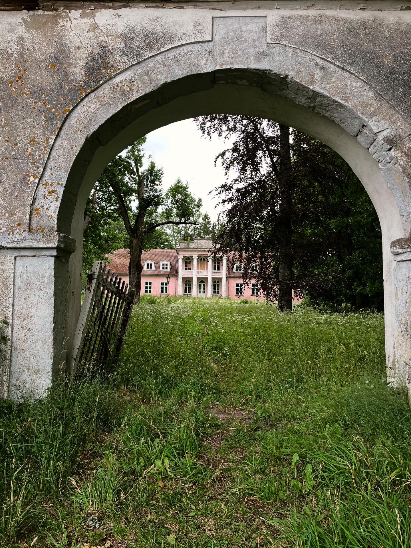 archway opening up to a green field with large pink building behind it