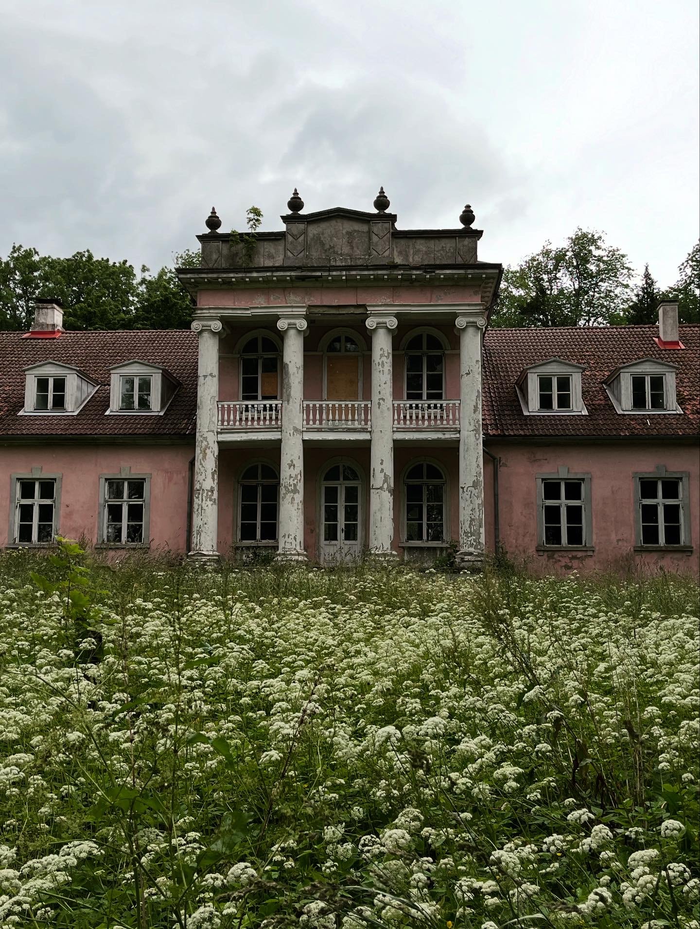 Old pinkish colored mansion in some disrepair, fronted by a two story columned porch