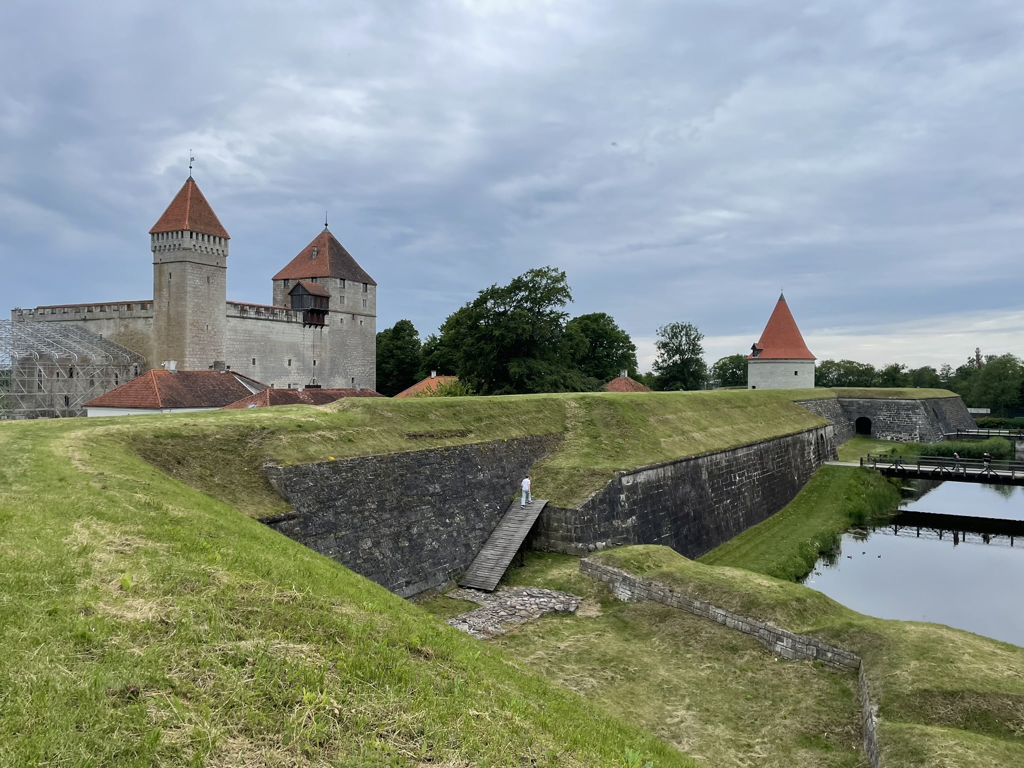 Castle fortifications of stop topped with turf, with castle towers in the distance