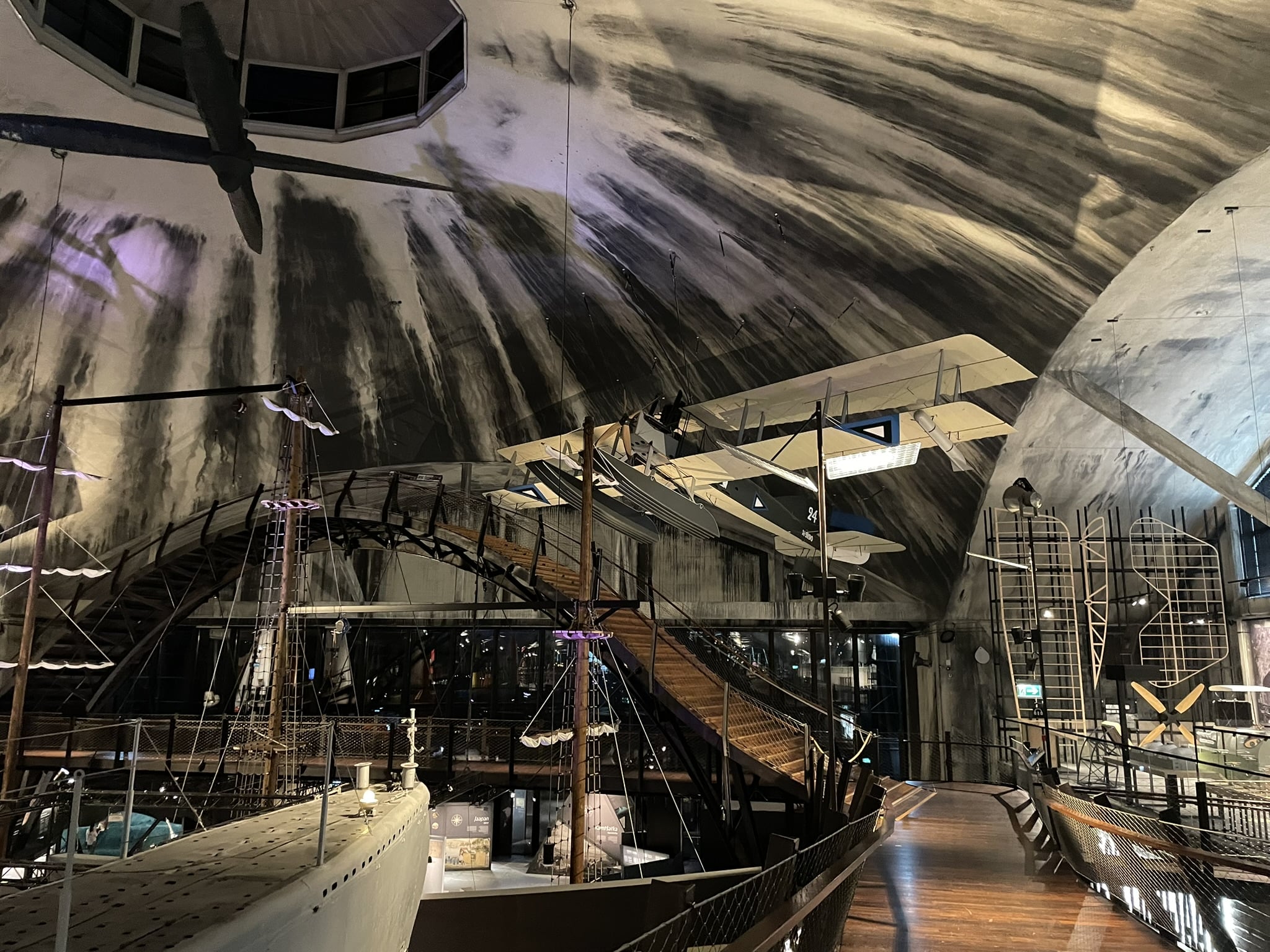 Cavernous space with two ship masts, a wooden arch bridge, and, hanging from the ceiling, a small seaplane