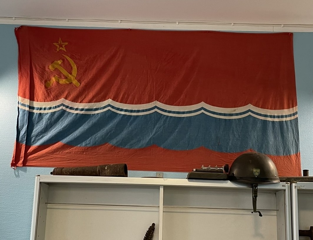 Red flag with hammer and sickle in the top left, and a blue and white wave pattern along the bottom
