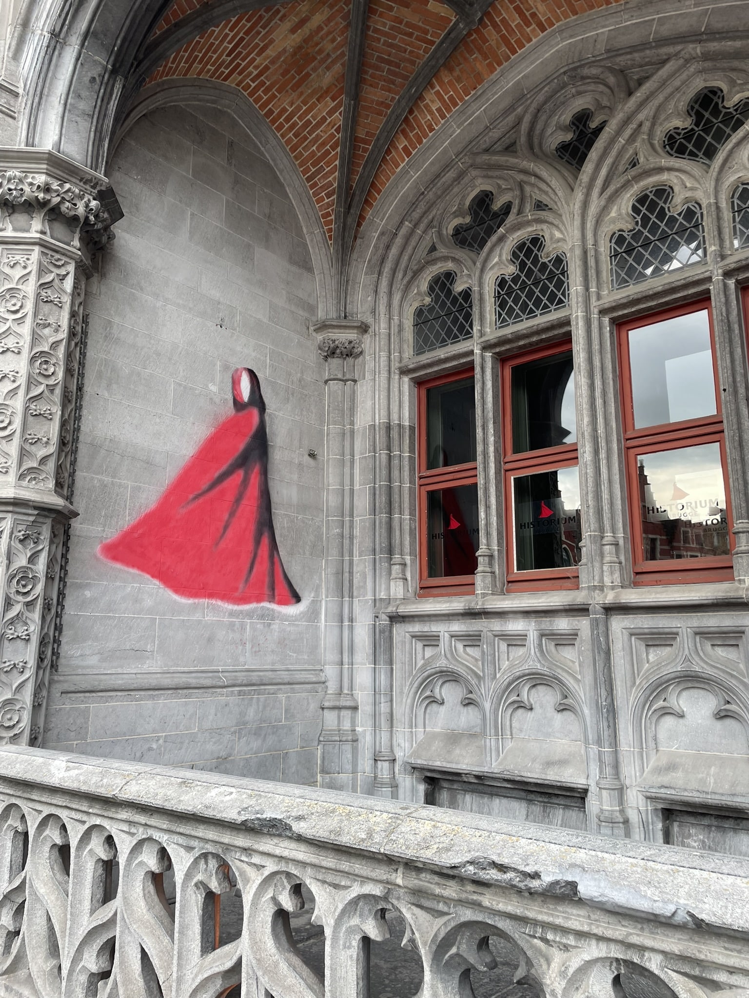 Gothic windows with an abstract figure of a red-cloaked woman painted on the wall