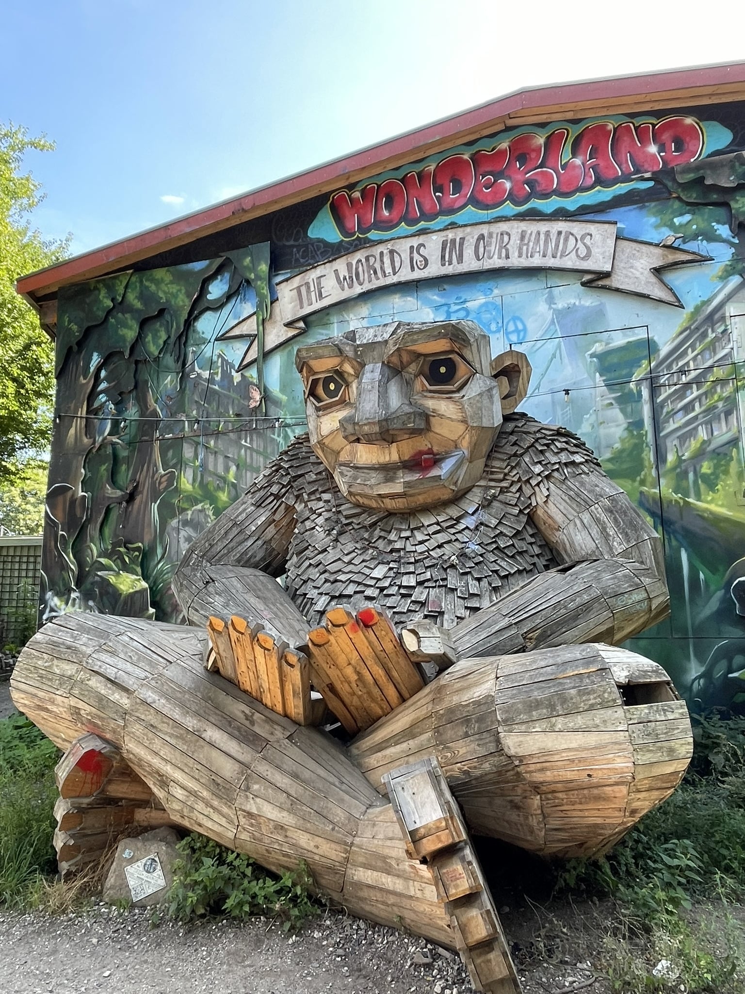 wooden troll statue against a building painted with the words: Wonderland: the world is in our hands