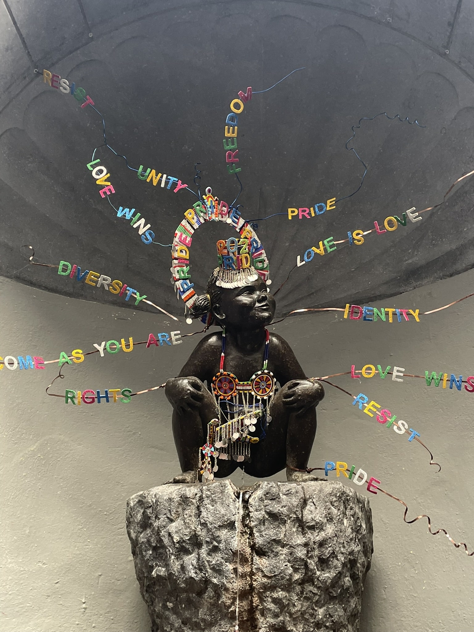 statue of a squatting, peeing girl, ornamented with pride decorations