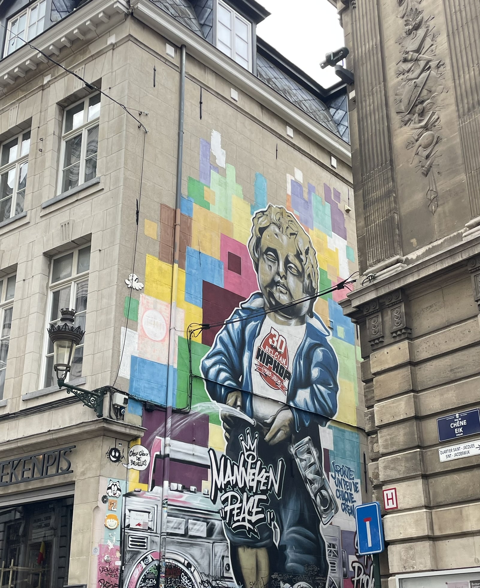street art on the side of a building showing manneken pis statue with "manneken peace" written below.