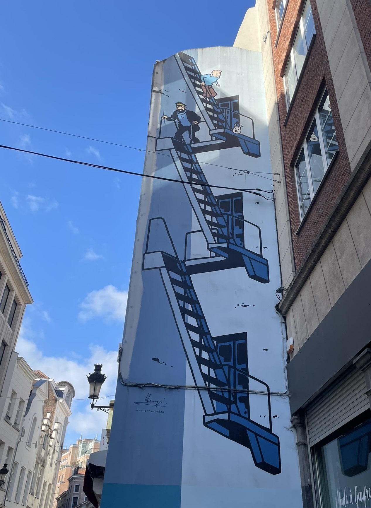 street art on the side of a building, depicting TinTin climbing up a metal staircase