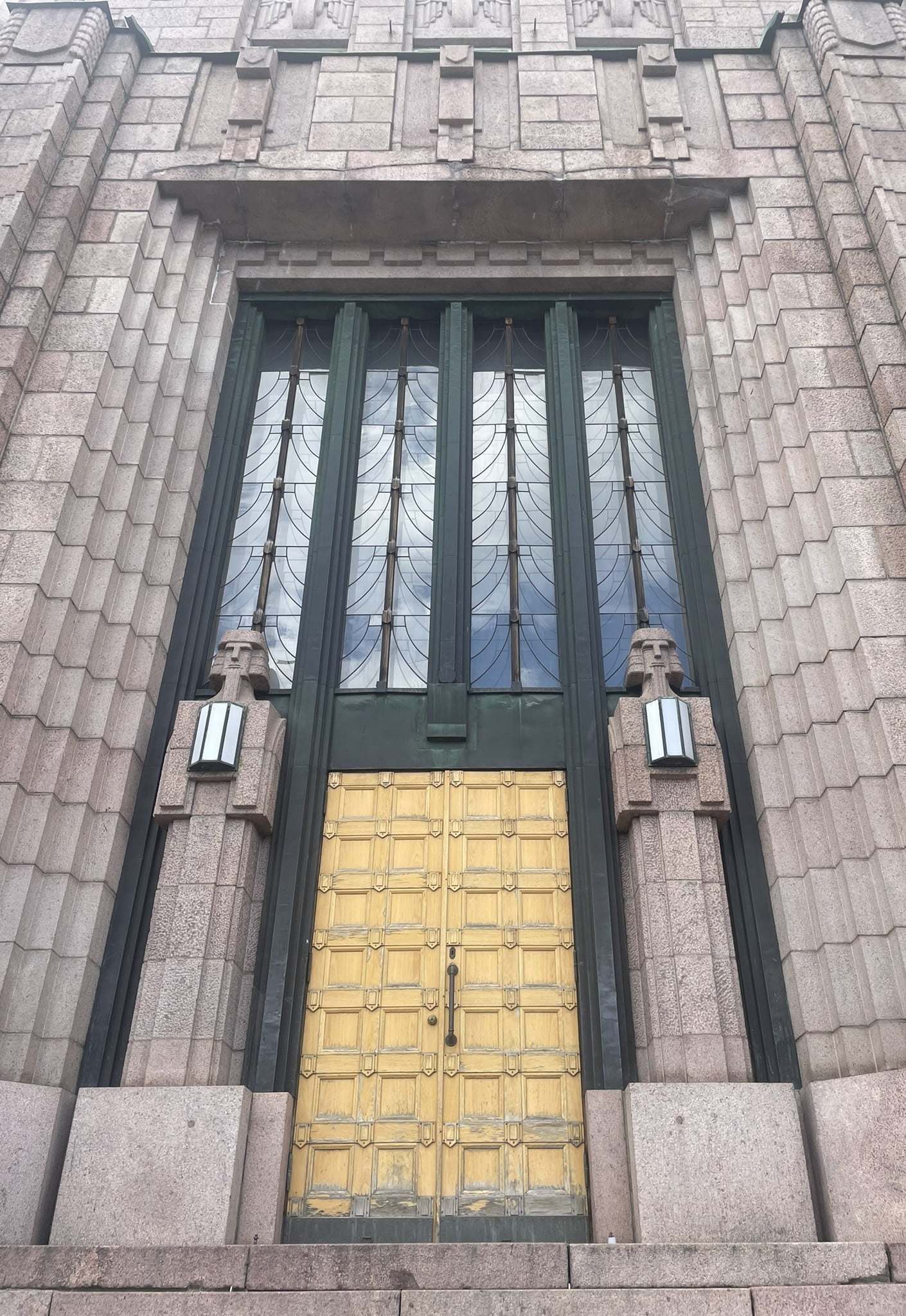 large golden door flanked by two figures holding rectangular lights