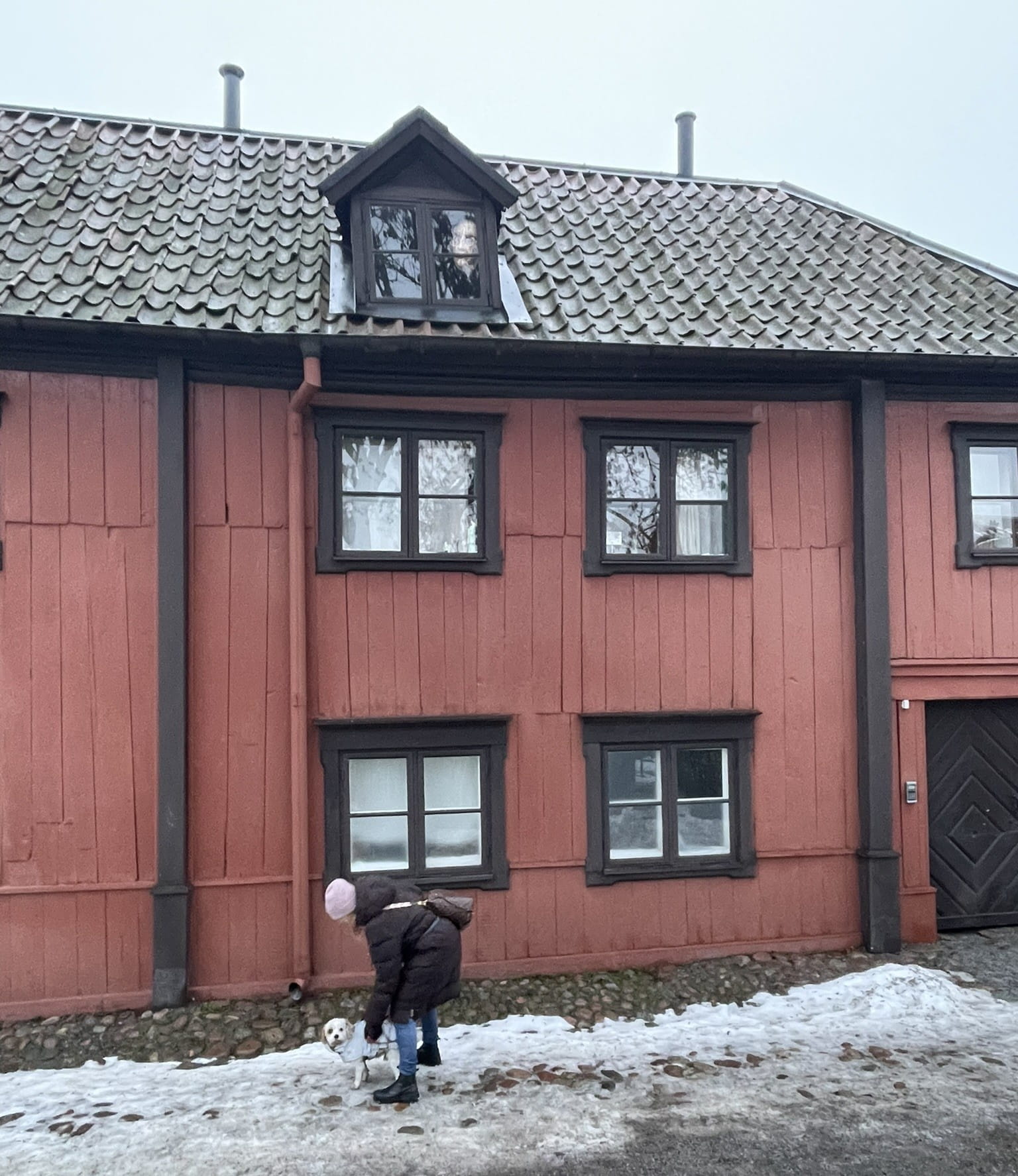Woman bending down towards s a small white dog in front of a wooden house