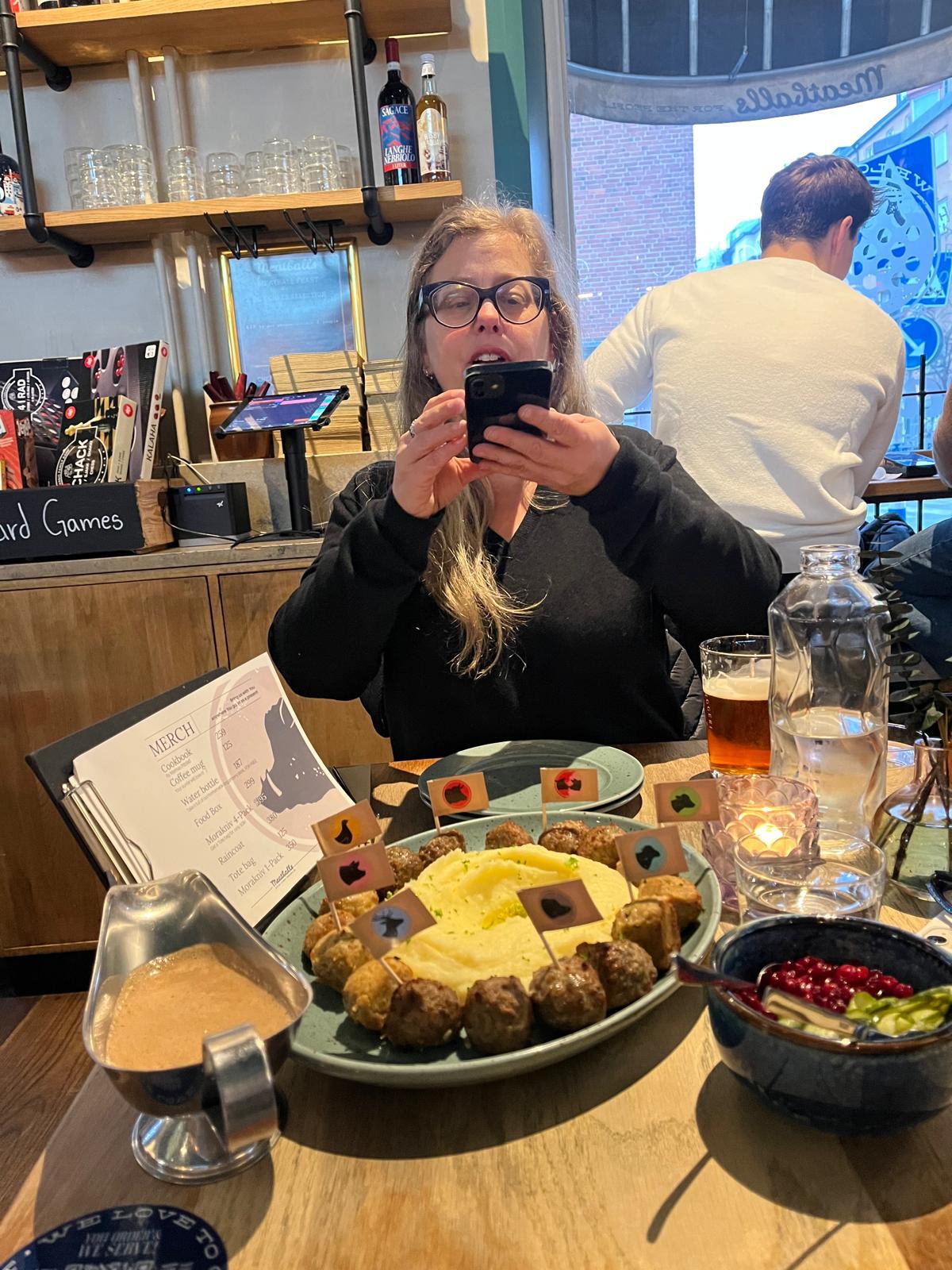 woman taking a photo of a plate of mashed potatoes and meatballs