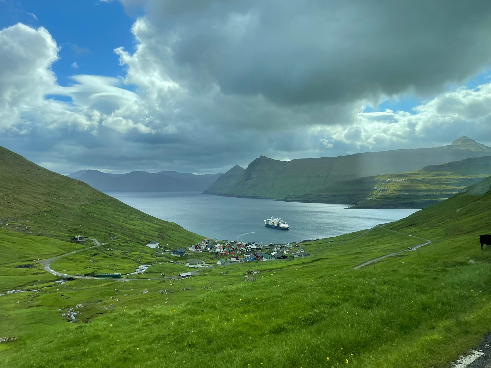 View from above of a fjord, green hills, and a ship in the distance