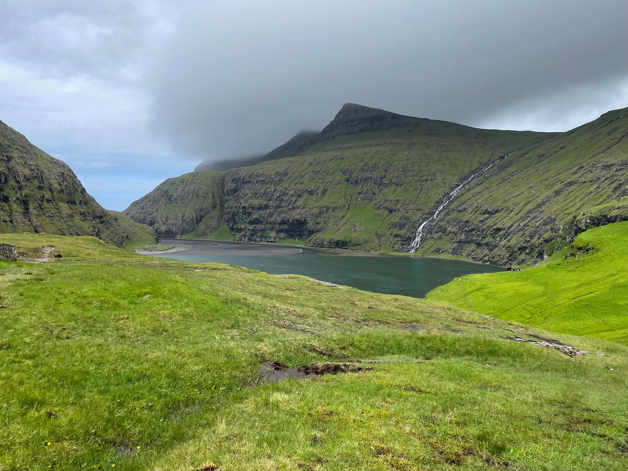 View of fjord and sloping green hills and a waterfall