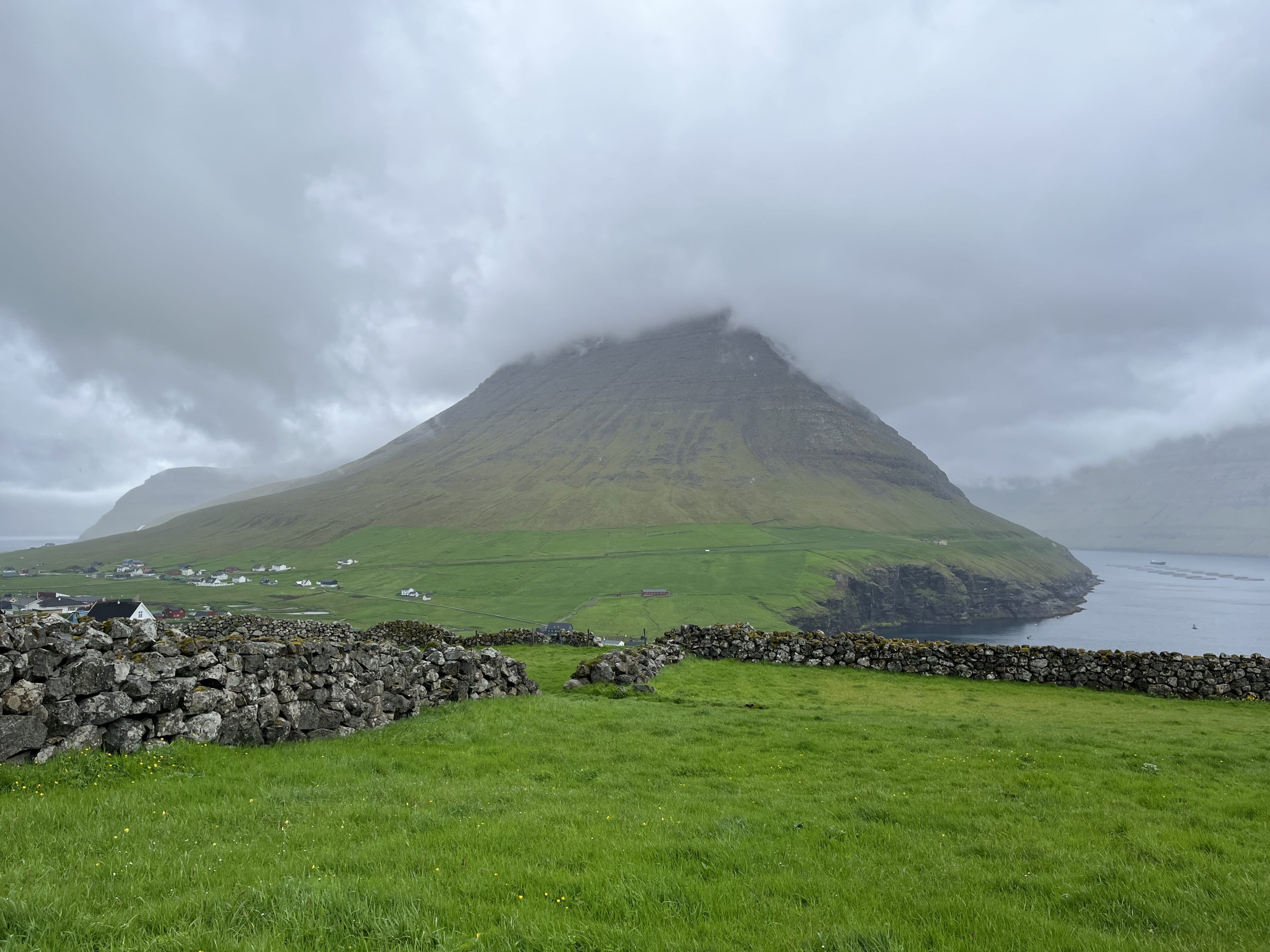 Green pasture and stone wall, with mountain and water in the distance