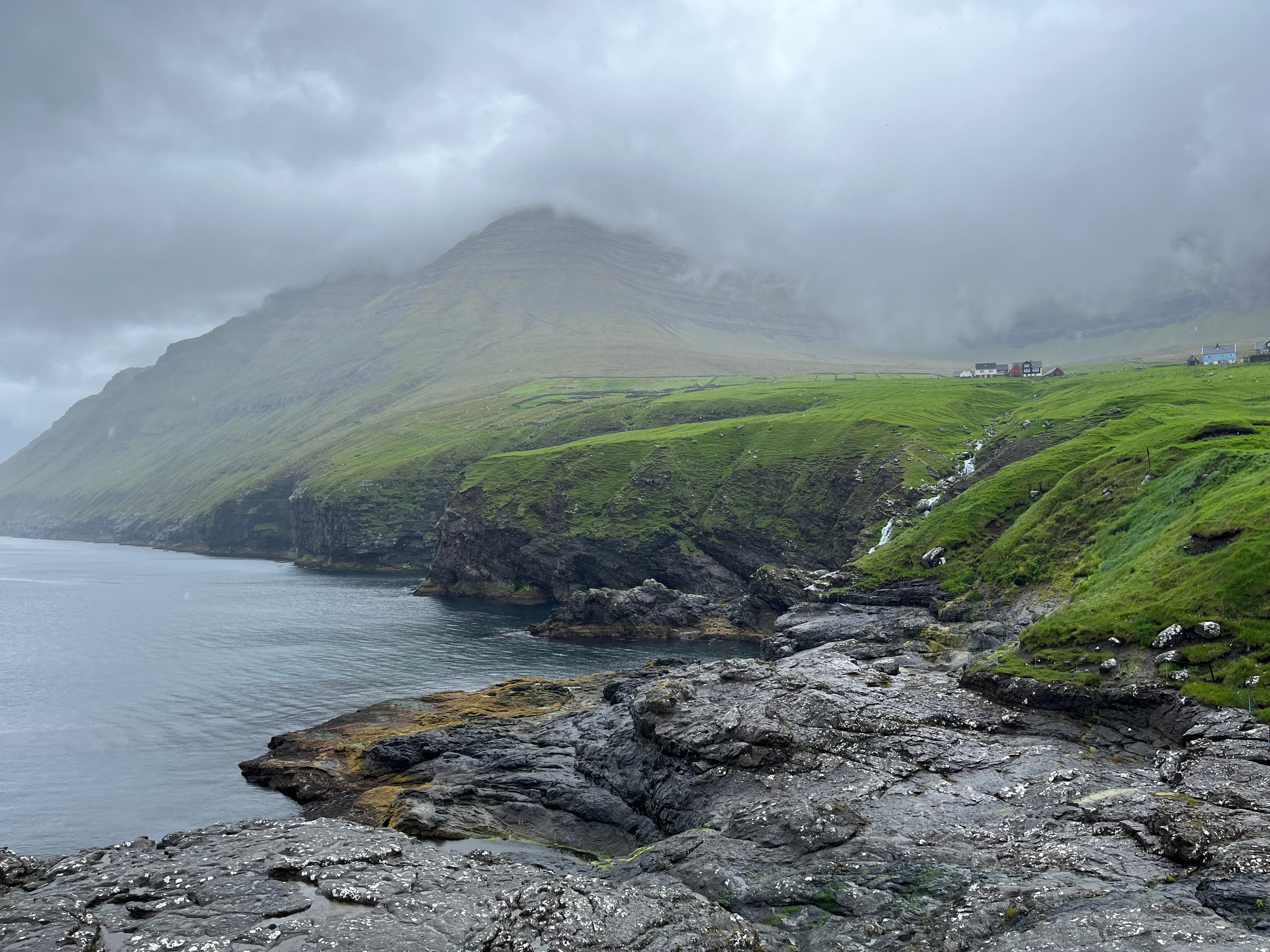 Black rock on the seashore with looming green mountains topped by fog