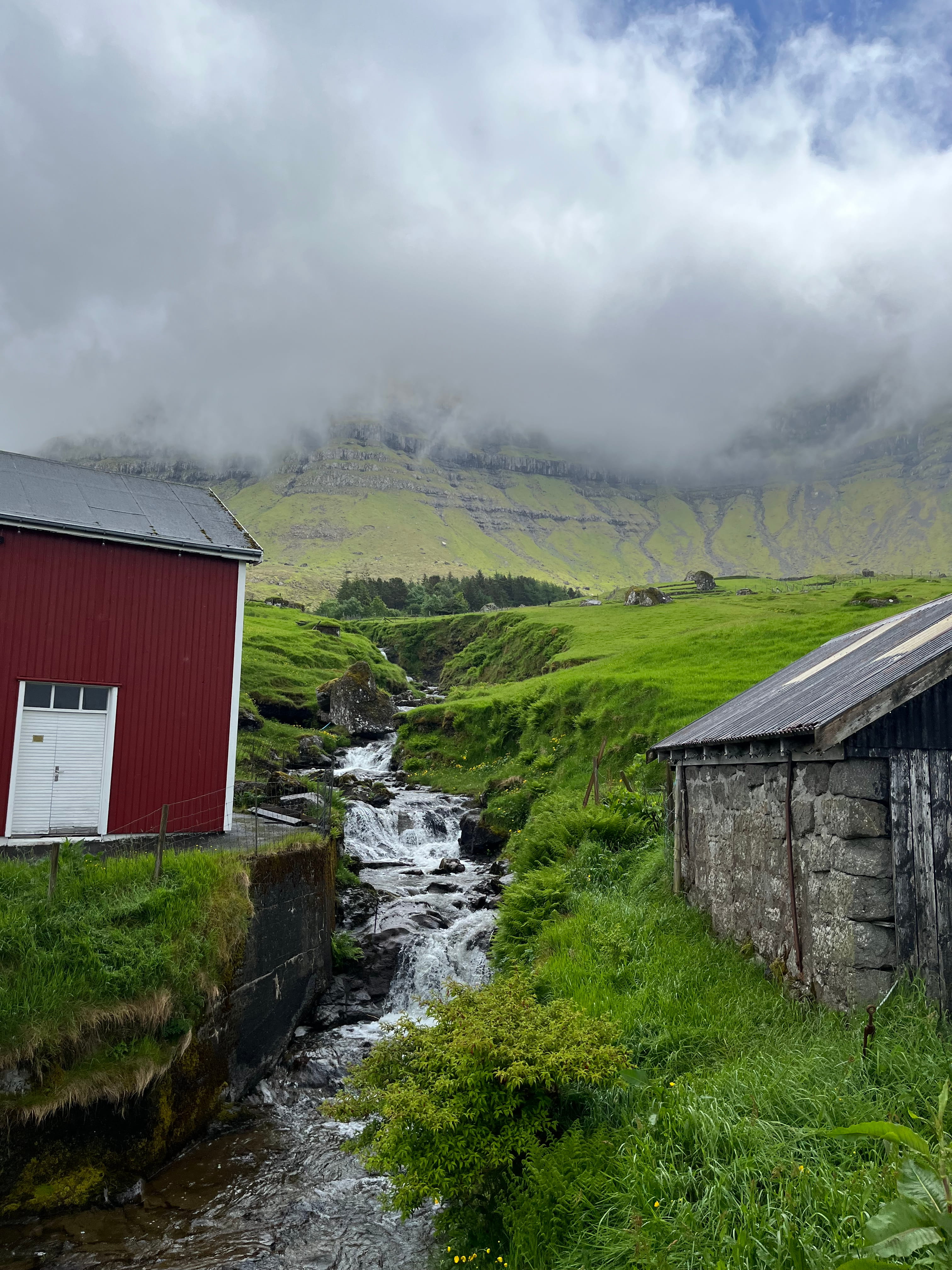 Foggy hills in the background with a stream running down between two farm buildings