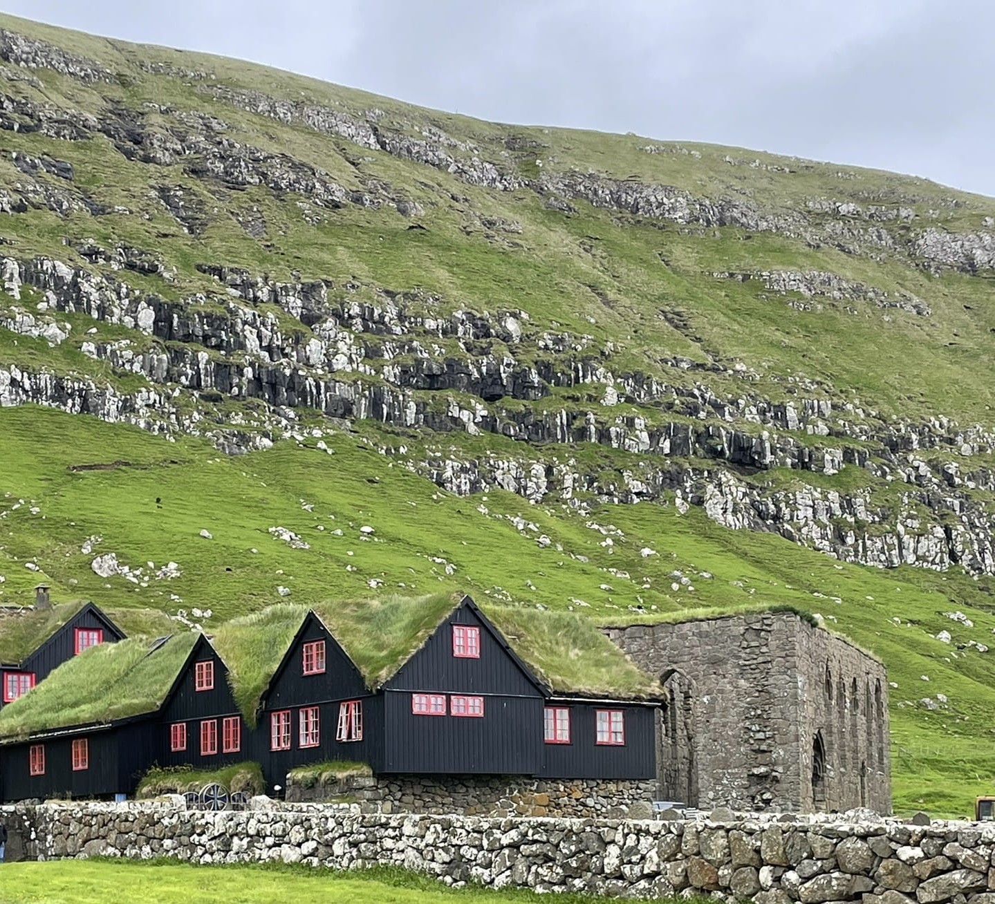 Turf roofed houses and a large stone building under rocky green hills