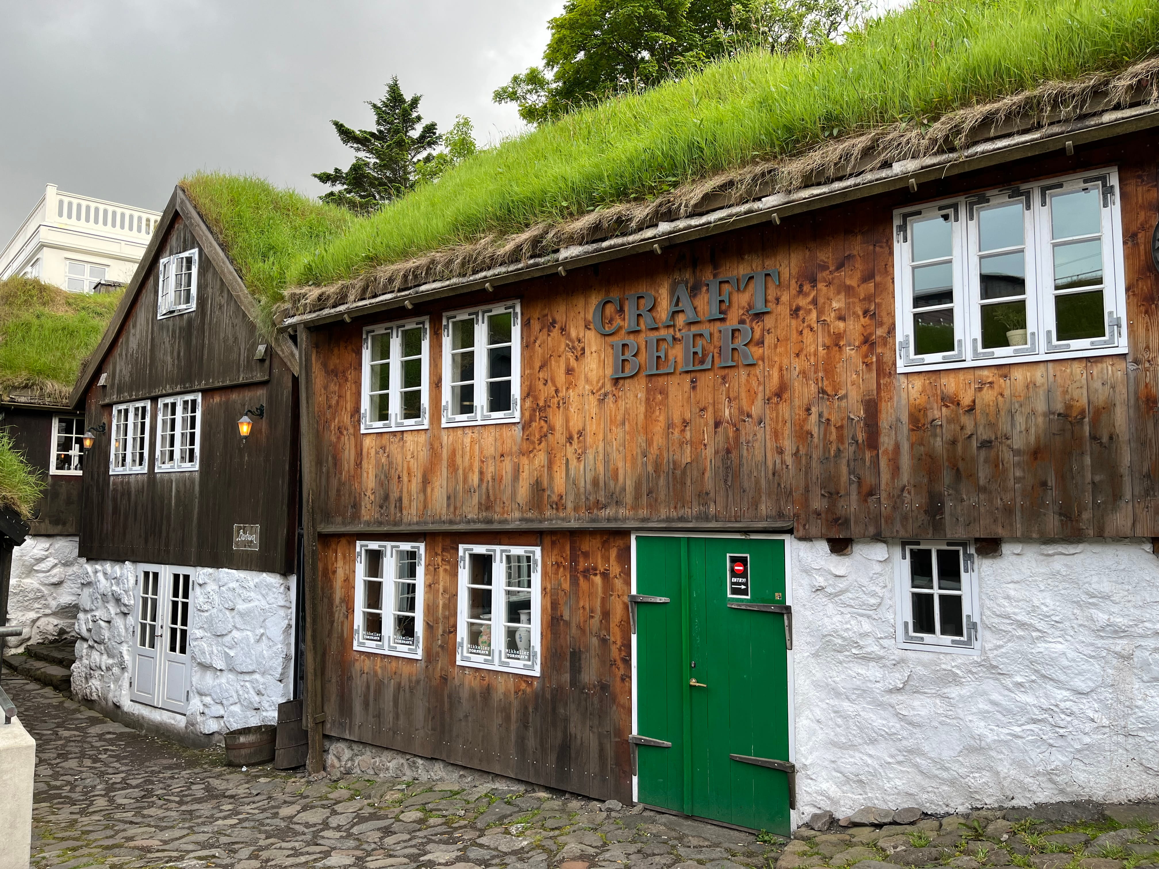 turf-roofed building with a green door and a sign that reads Craft Beer