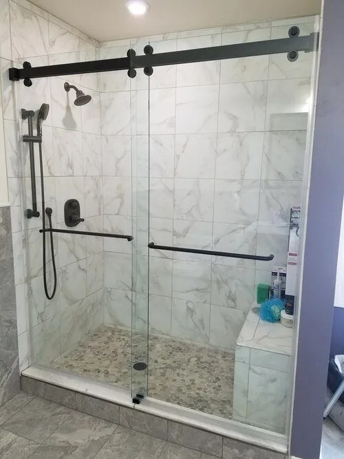 Frameless sliding glass shower door with matte-black hardware and marble-look wall tile