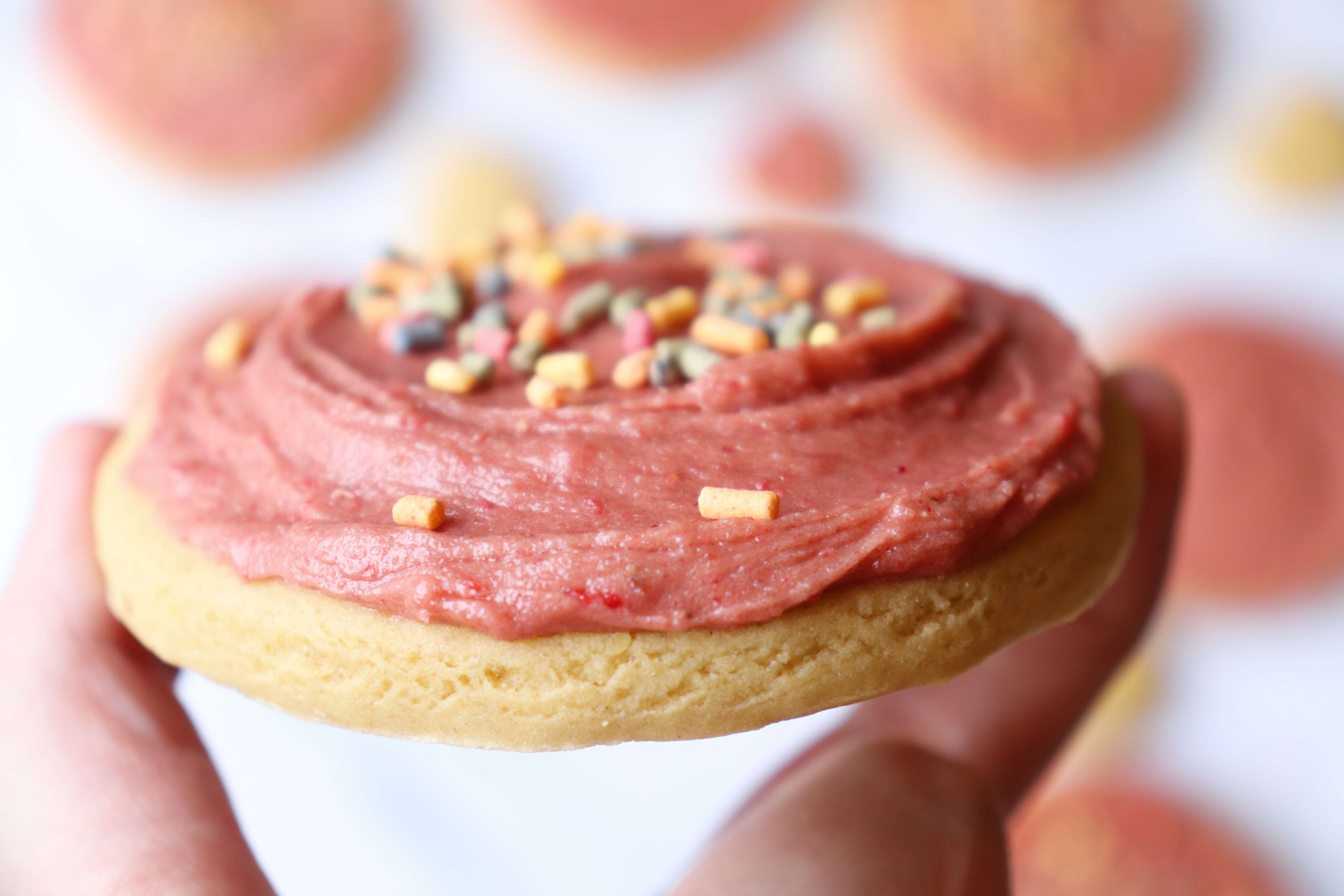 holding an einkorn flour sugar cookie with strawberry frosting and spinkles on top