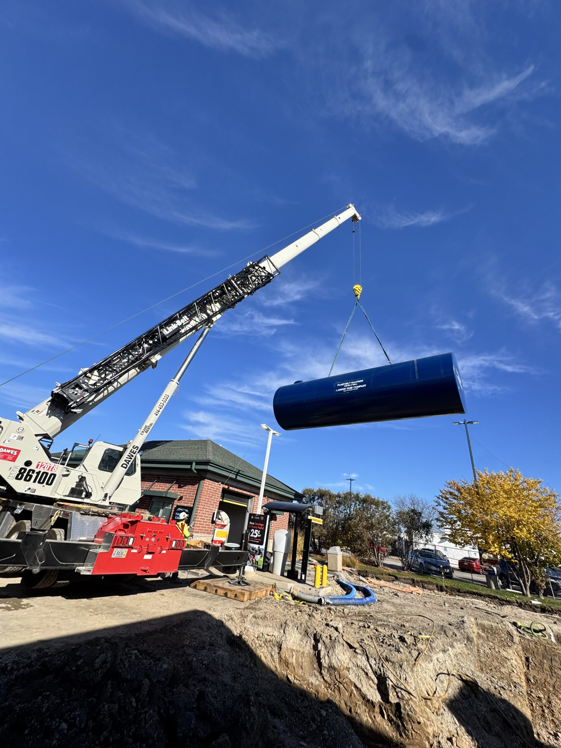 Crane lowering a new 10,000-gallon double-wall fiberglass underground fuel storage tank (UST) at a Shell gas station and Dunkin’ Donuts in Kenosha, Wisconsin – T&K Builders commercial tank replacement project