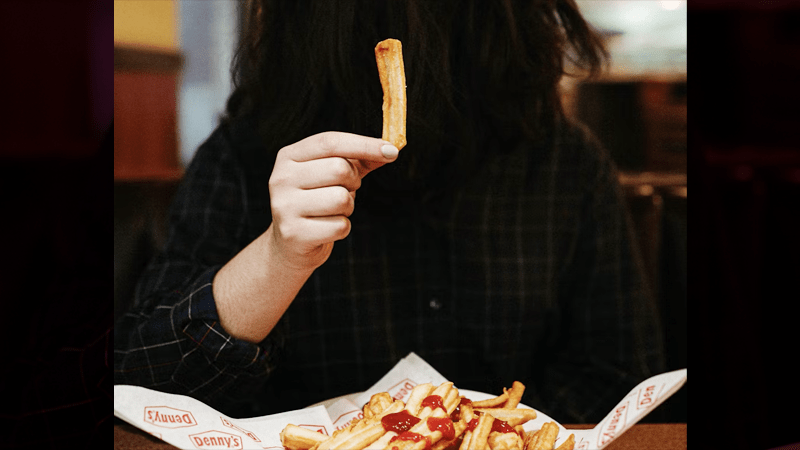 A close-up of a person holding a single french fry, symbolizing the connection between mindful eating and faith-based health practices.