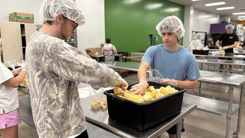 Volunteers package corn at a food bank, highlighting the importance of data in addressing food insecurity and resource allocation.