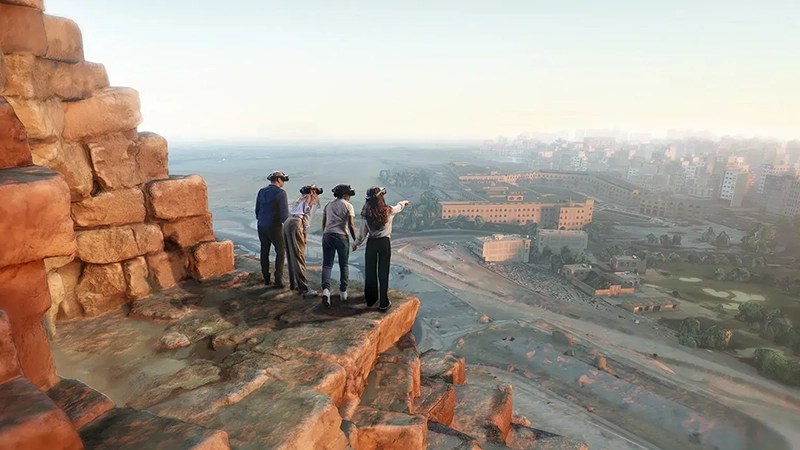 Four individuals wearing VR headsets stand on the stepped upper part of an ancient stone pyramid, overlooking a sprawling modern city under a hazy sky.