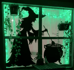 Large witch and cauldron window silhouette glowing green across a double front window.