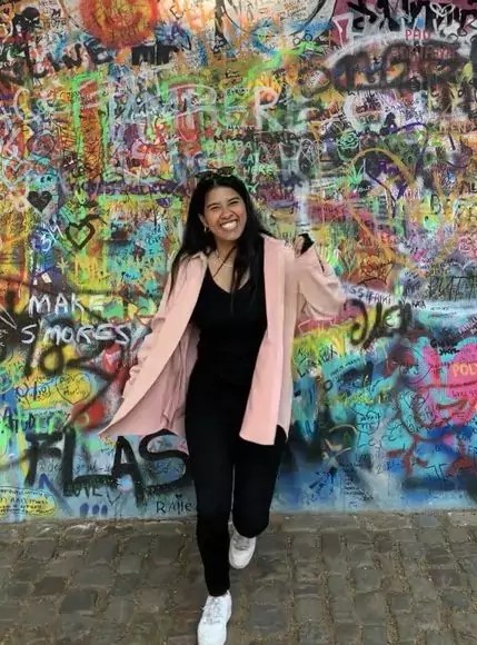 Joyce Lopes, Software Engineer at ToffeeX team. Joyce is stood infront of a wall of grafitti and is smiling