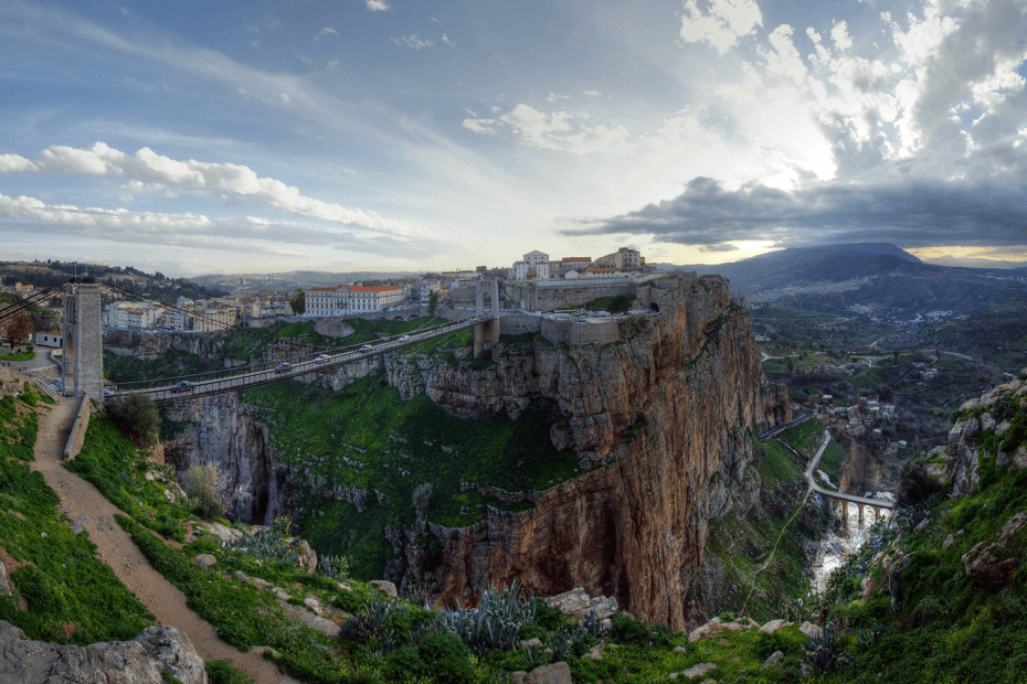 View of a buildings and a bridge sitting over cliffs with sunset in the background