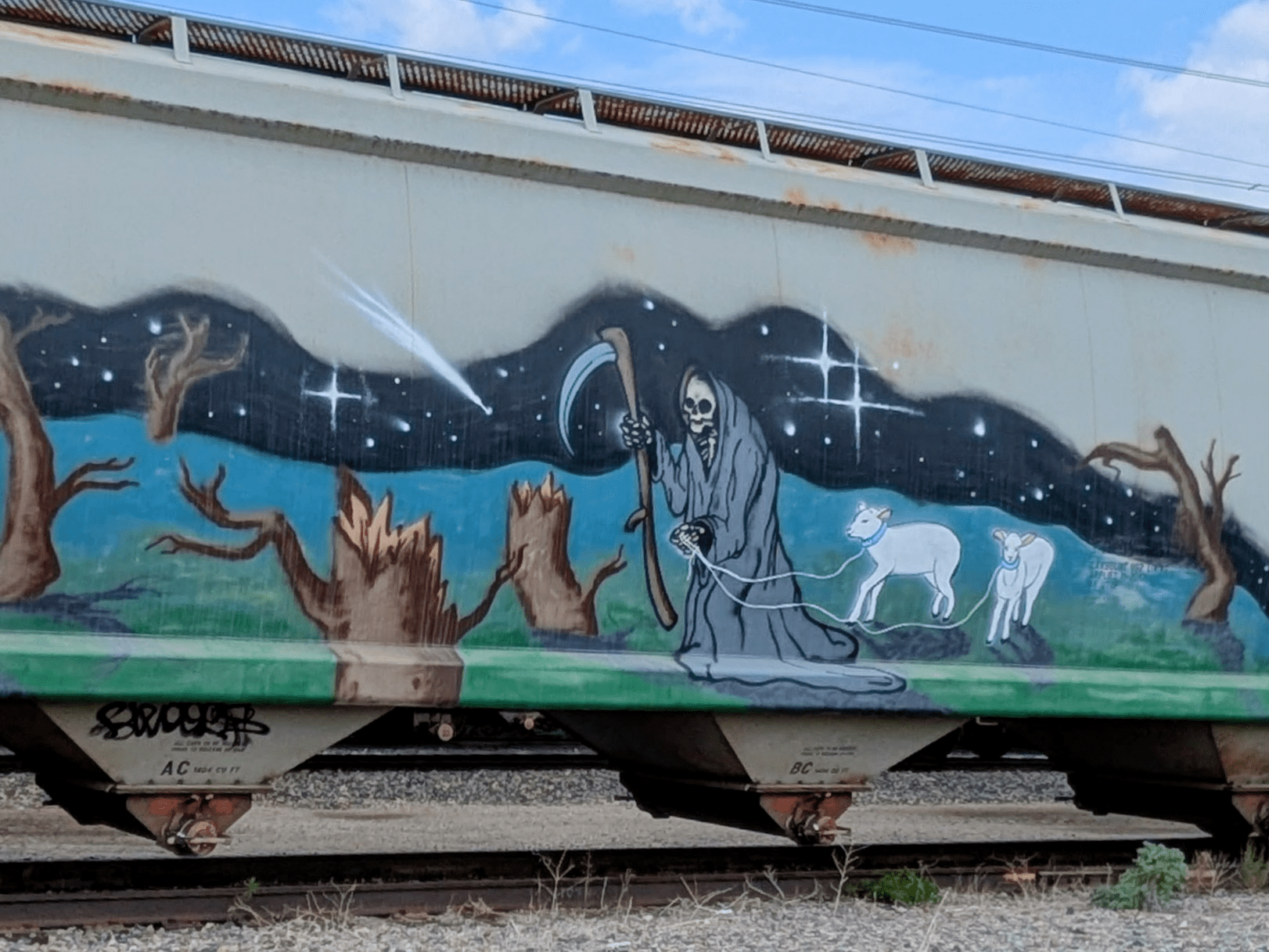A graffiti artwork on the side of a train car depicts a grim reaper holding a scythe and leading two sheep through a desolate landscape of dead trees under a starry night sky with a comet.