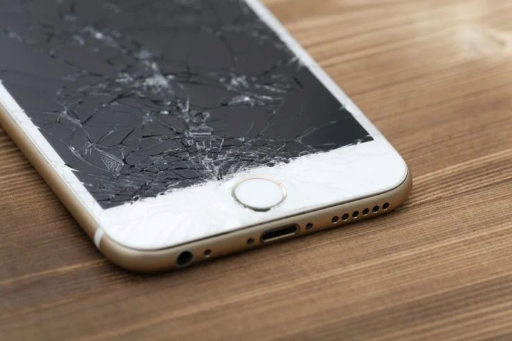 An iPhone with a shattered screen lying on a wooden table