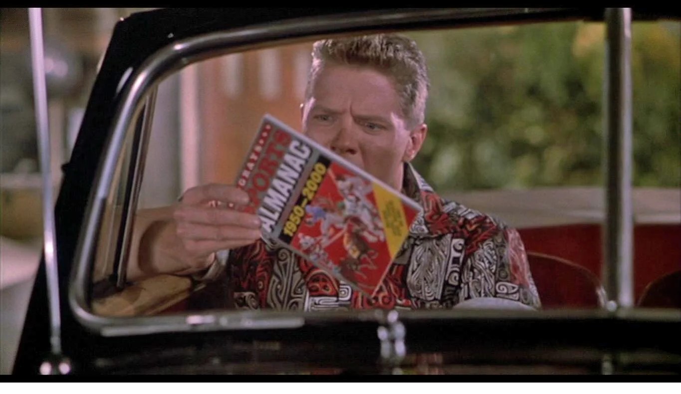 Scene from Back to the Future Part II: a man in a car holding up the "Grays Sports Almanac 1950-2000"