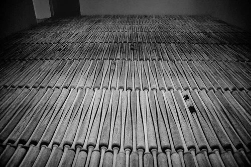 Black-and-white photo of hundreds of baseball bats laid in rows across a museum floor