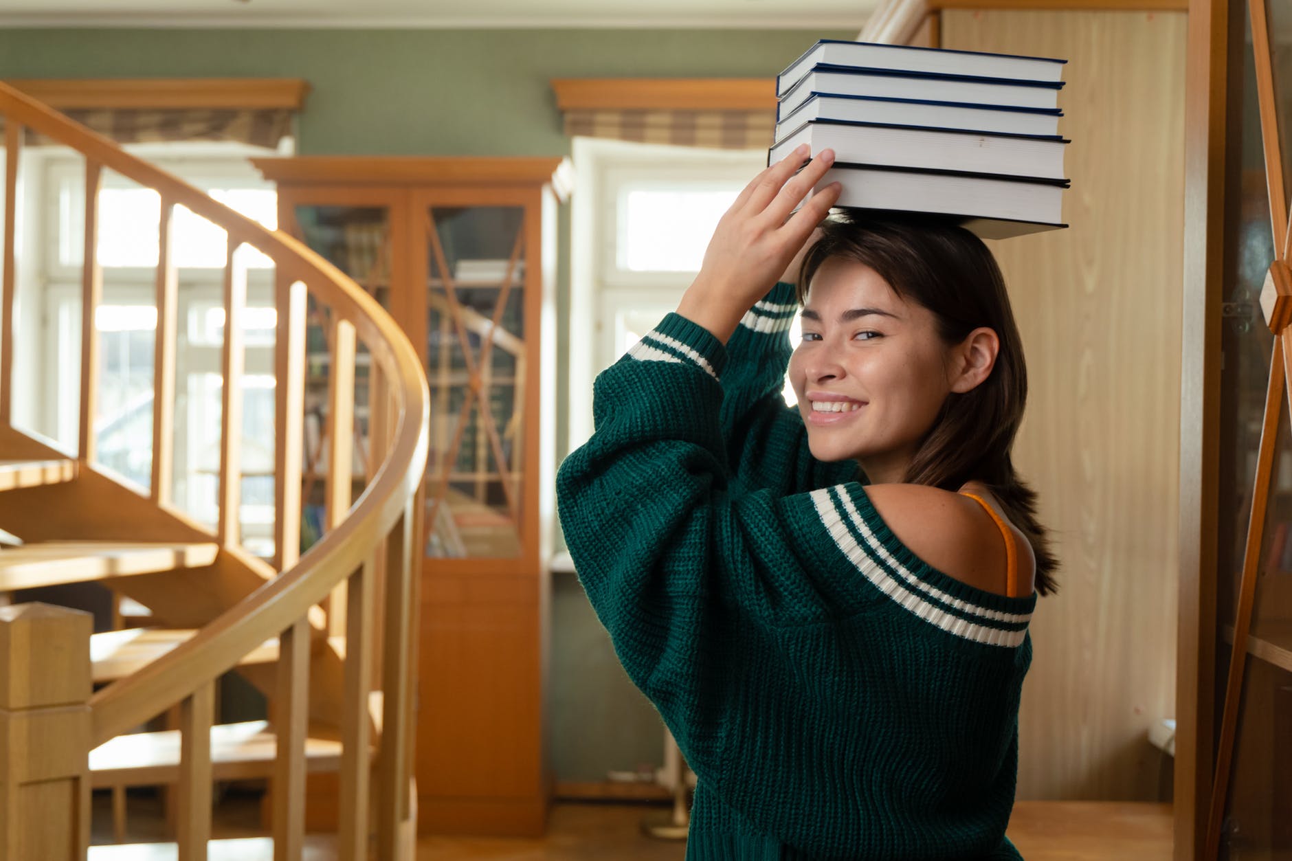 a woman smiling while holding a pile of books on her head