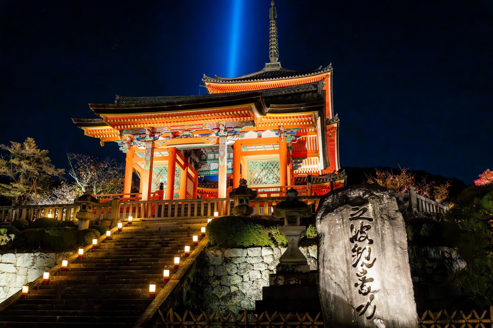 夜間點燈的朱紅寺院門樓，階梯旁立著石碑