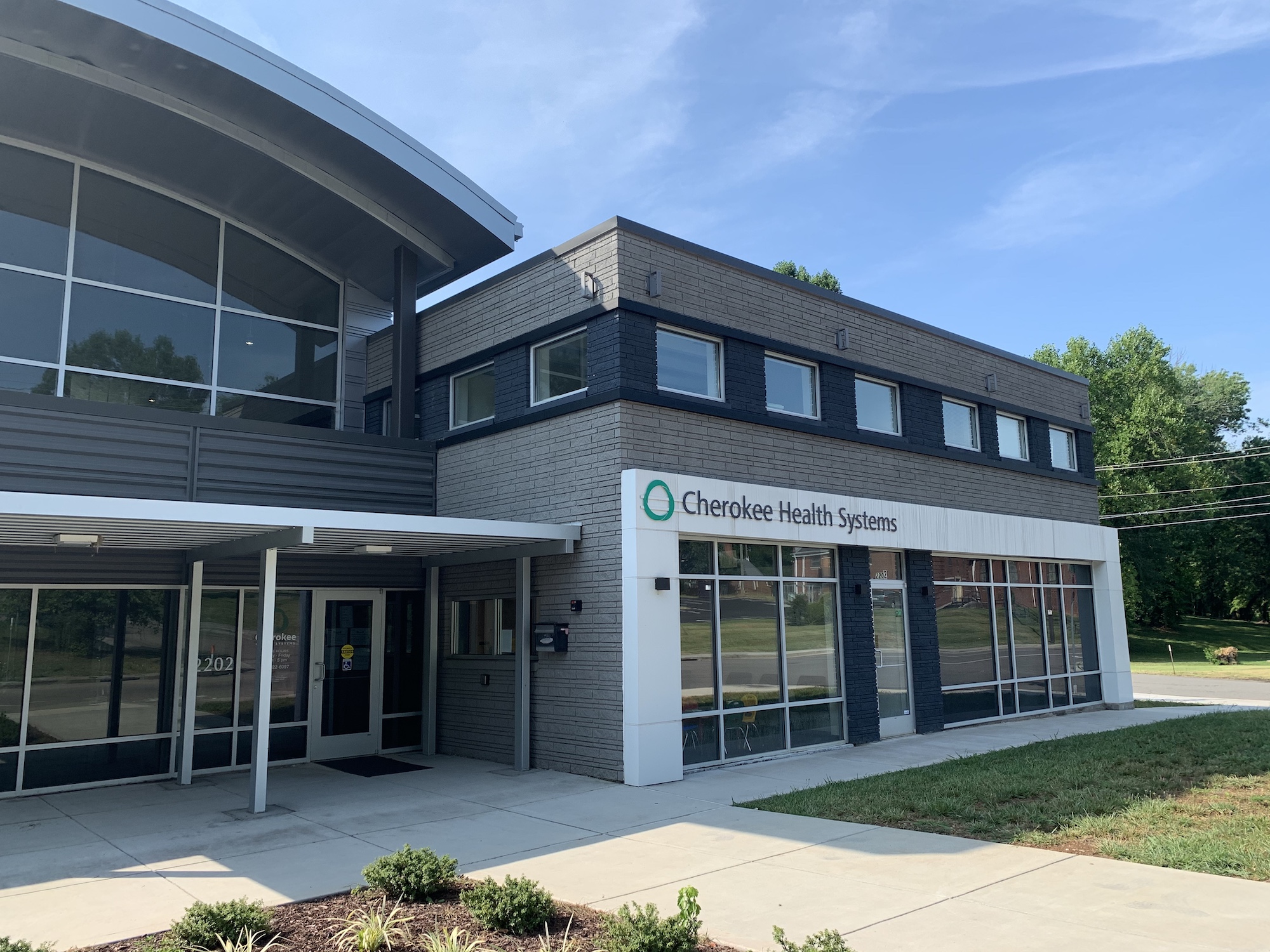 Exterior view of Cherokee Health Systems building with a mix of brick and metal design, large windows, and surrounding greenery.