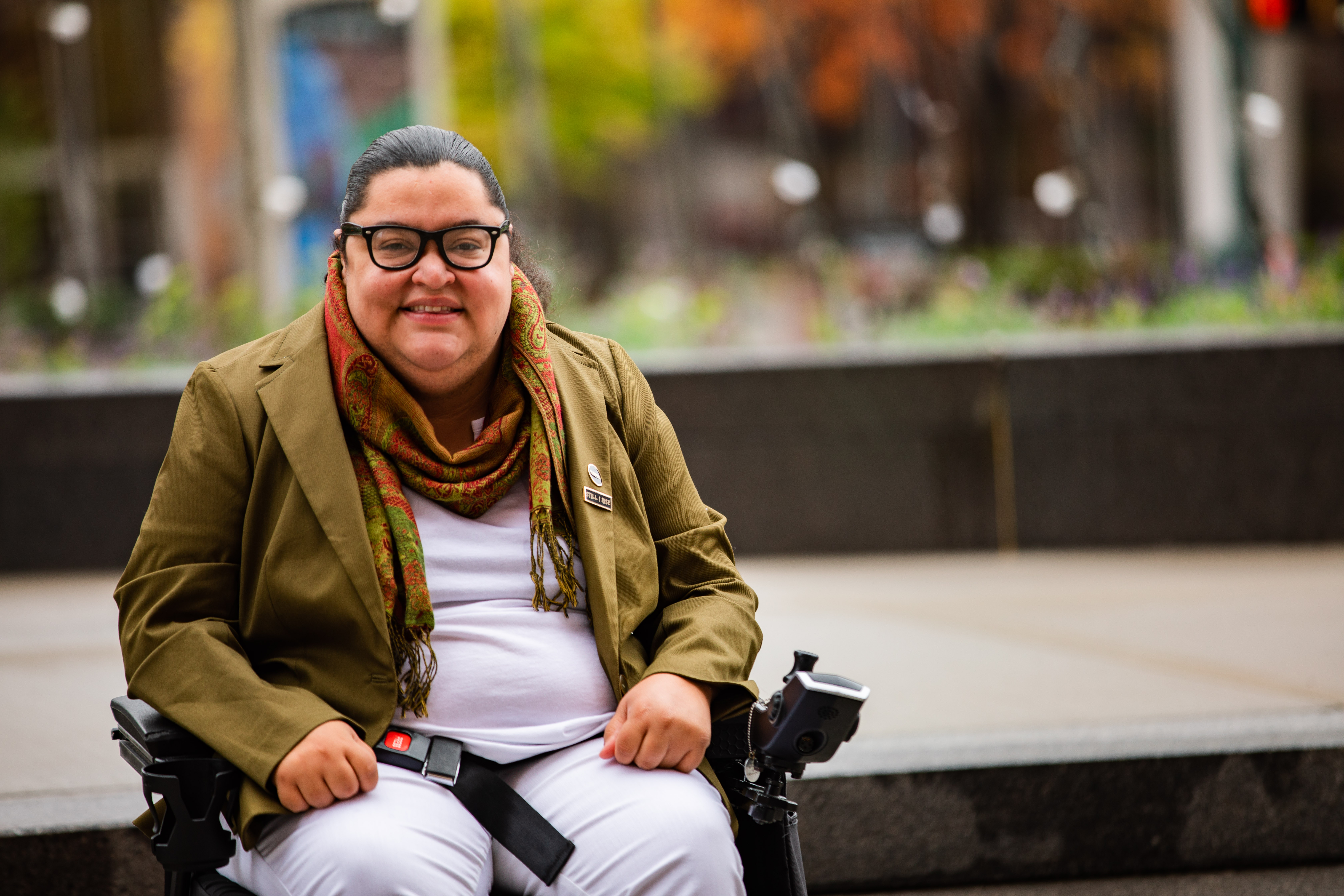 Person in a wheelchair wearing a green blazer and scarf.