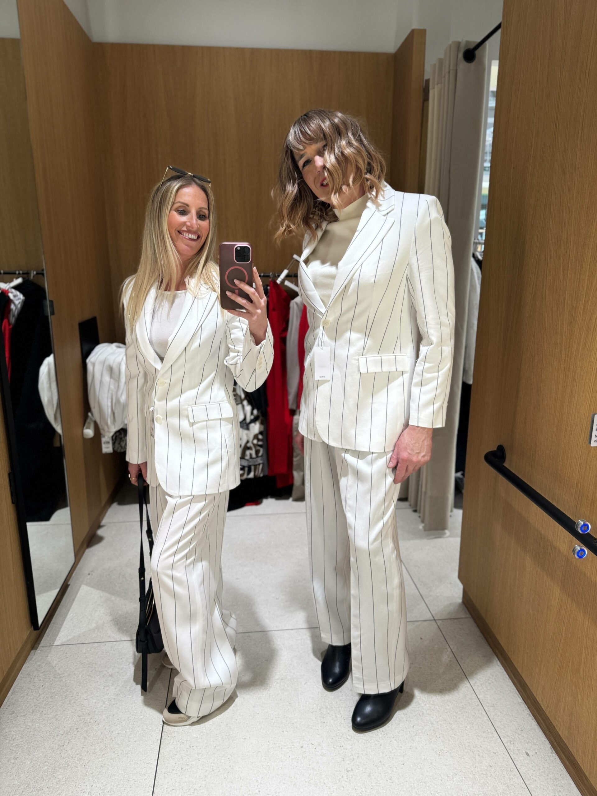 Jennifer de Transbeauté prend un selfie avec une cliente transgenre dans une cabine d’essayage. Elles portent toutes deux un tailleur blanc à rayures noires. L’ambiance est complice et élégante.