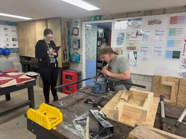 A student is checking and maintenancing construction hand tools, whilst another watches on ensuring safety protocols are followed.